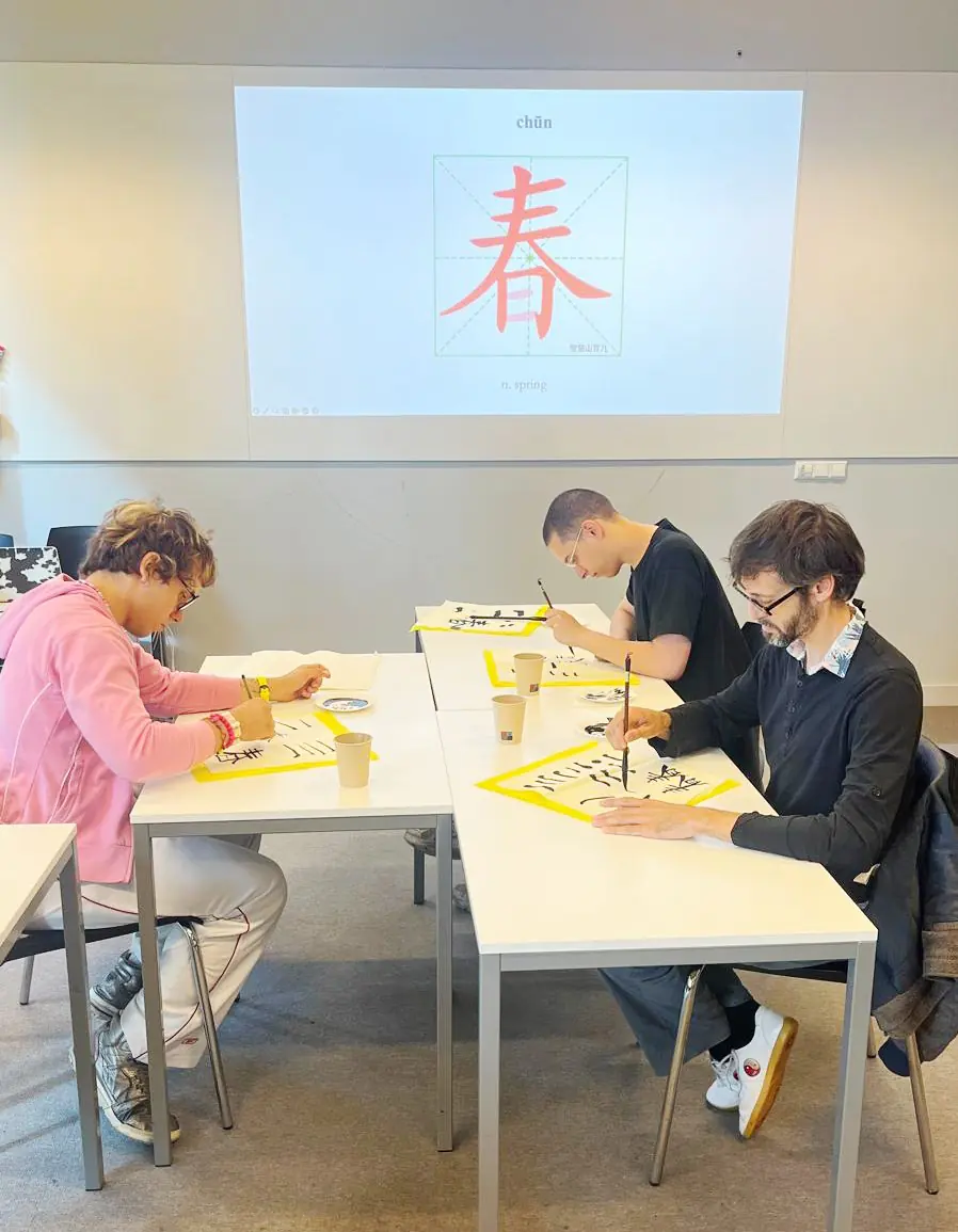 Chinese stroke order: learners writing 春 (spring) with a brush, with its pinyin and practice grid on the screen