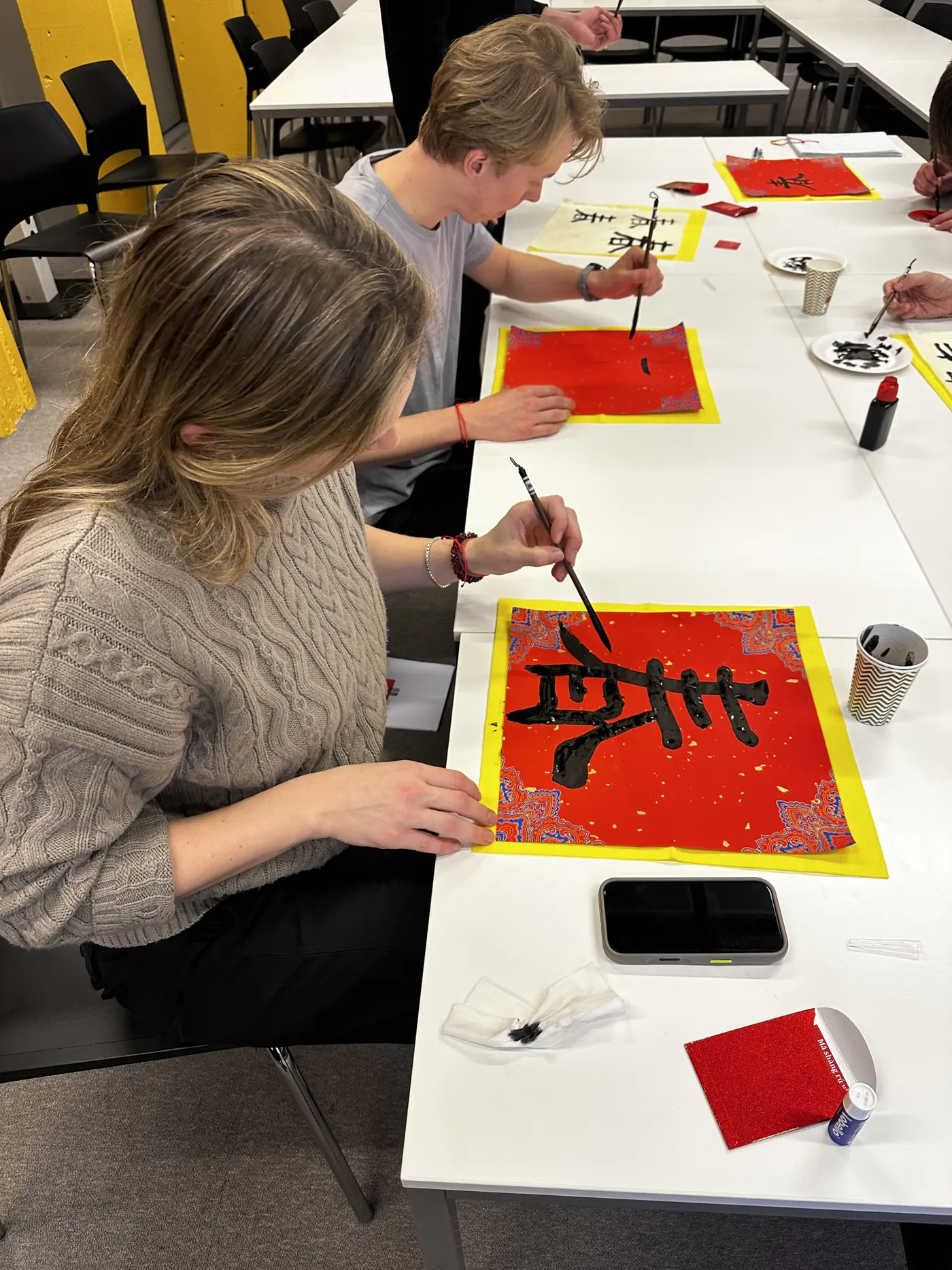 书法课：一位学员用毛笔在红纸上写字